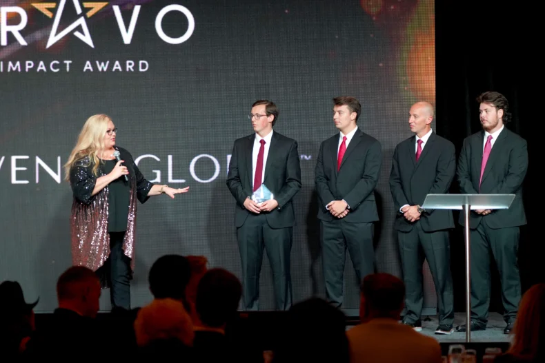 Aspen Emry speaks from stage: Bravenly Global has received the 2026 Bravo Impact Award and #40 on the DSN Global 100 (product-focused companies)