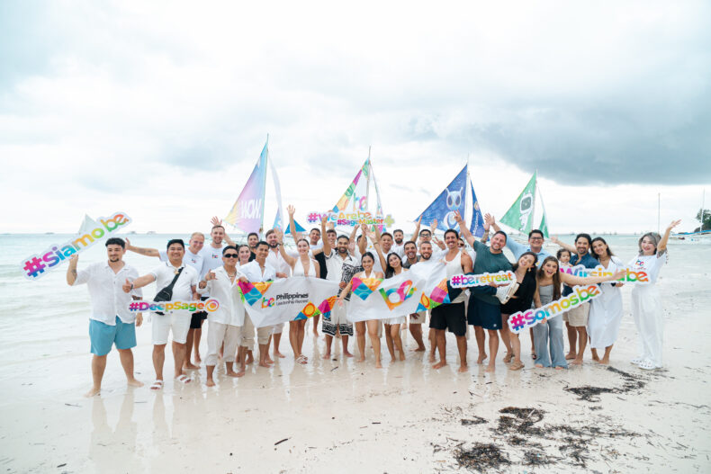 BE leaders gathered on the beach in the Philippines holding colorful retreat banners