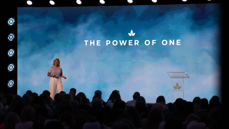 Brittany Beck delivering a keynote speech on stage at Bravenly Global Summer Success Summit 2025