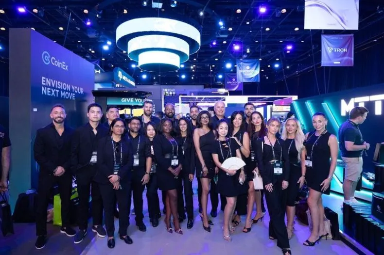 Group photo of the C1 team at their TOKEN2049 Dubai booth under bright lights and sponsor banners