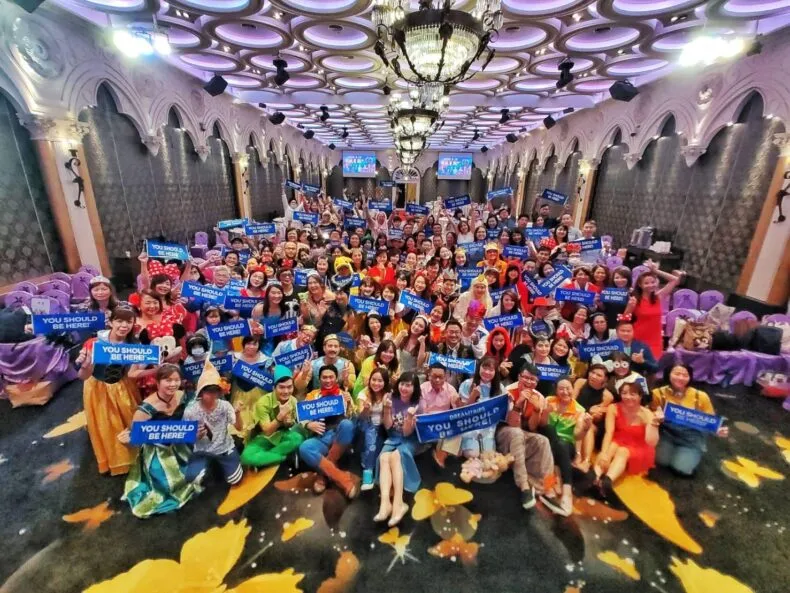 Group of DreamTrips members gathered indoors holding “You Should Be Here” signs