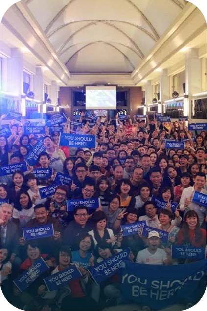 DreamTrips global community holds “You Should Be Here” signs during a large group event.