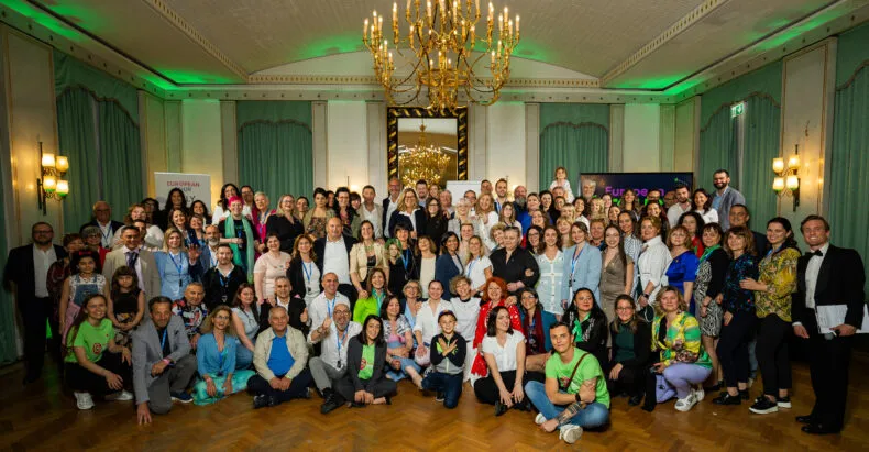 Large Greenway crowd gathered in an elegant hall with chandeliers, smiling and celebrating during the Italy leg of the European Tour.