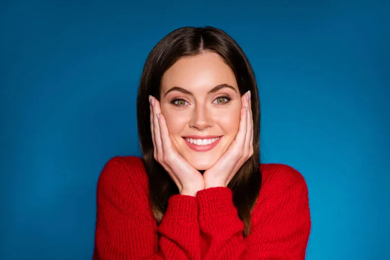 Smiling woman in a red sweater posing against a blue background