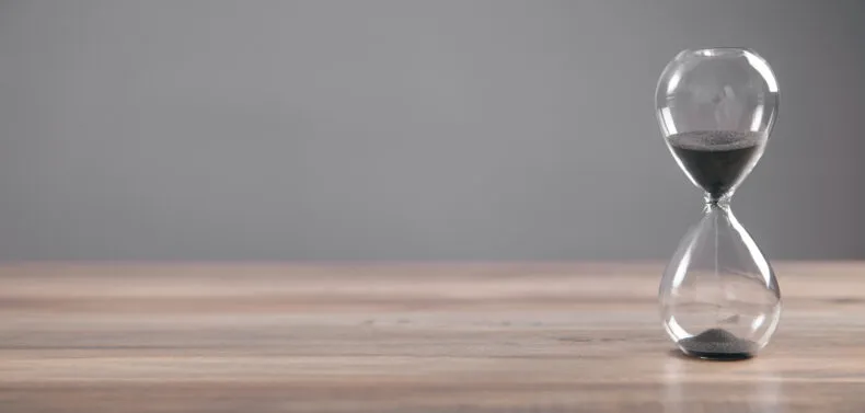 Hourglass with black sand flowing on a wooden table