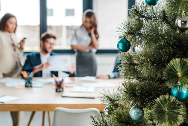 Christmas tree in an office with people talking in the background during a holiday work setting