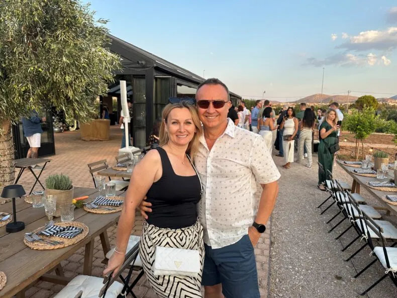 János Sztruhár and his wife smiling together outdoors at a dinner event surrounded by guests.