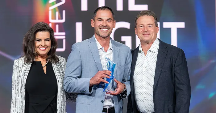 Joe Navarro accepting a LifeWave leadership award on stage alongside LifeWave President Meredith Berkich and LifeWave Founder David Schmidt