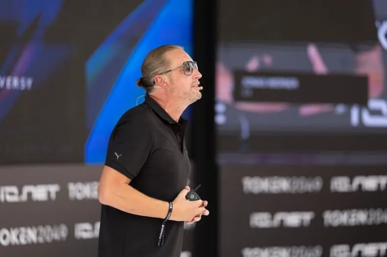 Close-up of Jonas Werner speaking on stage with microphone and slide background