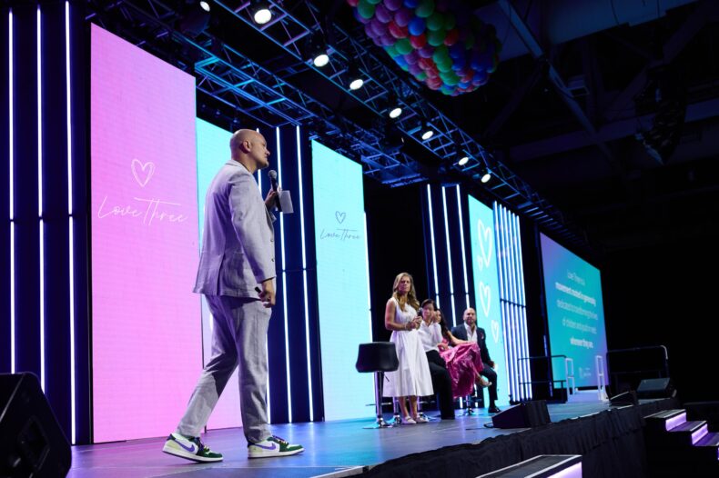 THREE International executive presenting the Love Three initiative on stage at a global convention