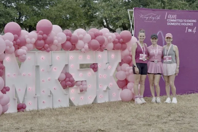 Three Mary Kay MK5K 2026 participants wearing race medals beside the pink MK5K event display