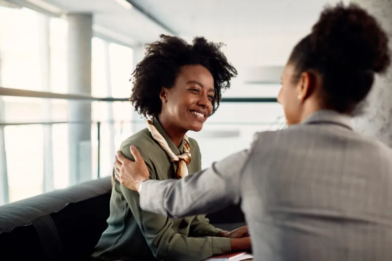 Two women having a supportive conversation, one with a hand on the other’s shoulder