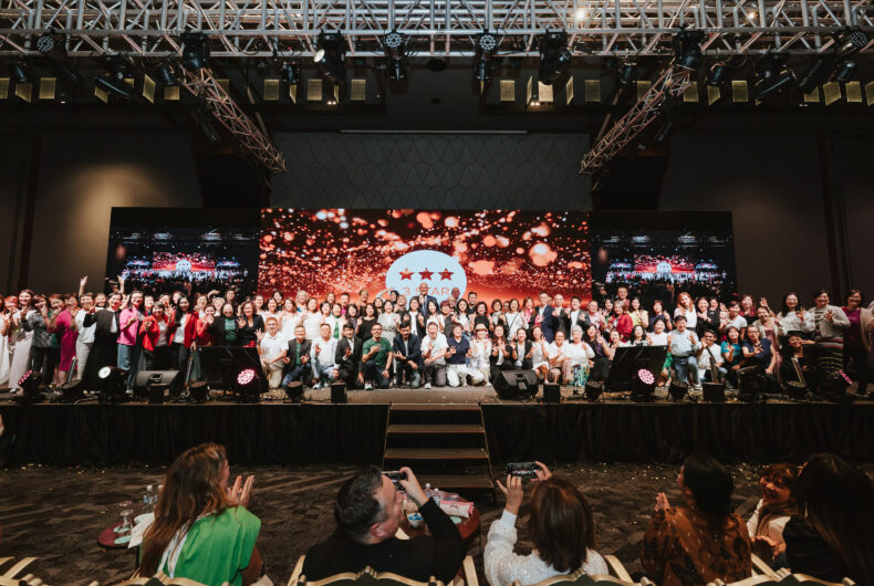 Group photo of THREE Brand Ambassadors and leaders onstage at an APAC recognition event with festive lighting