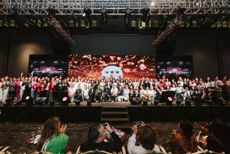 Group photo of THREE Brand Ambassadors and leaders onstage at an APAC recognition event with festive lighting