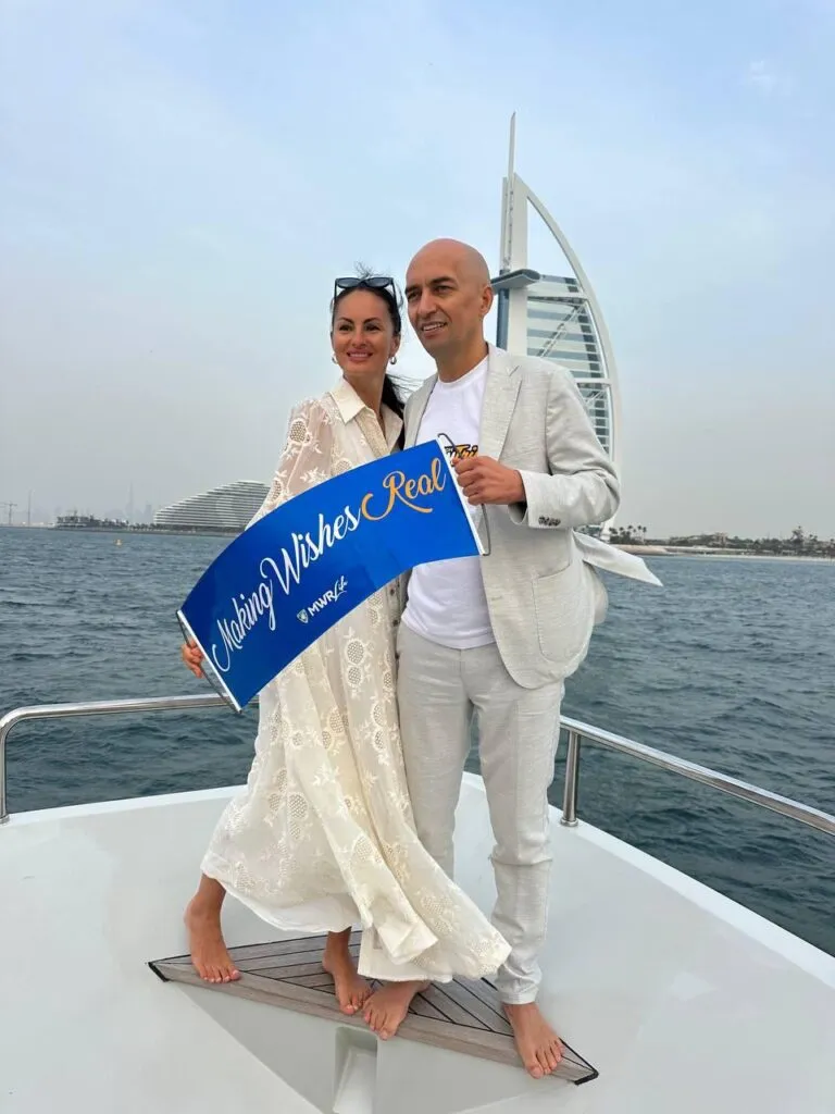 Viktor Vysotskyi and his wife Ewya holding a “Making Wishes Real” MWR Life banner on a yacht in Dubai with Burj Al Arab in the background.