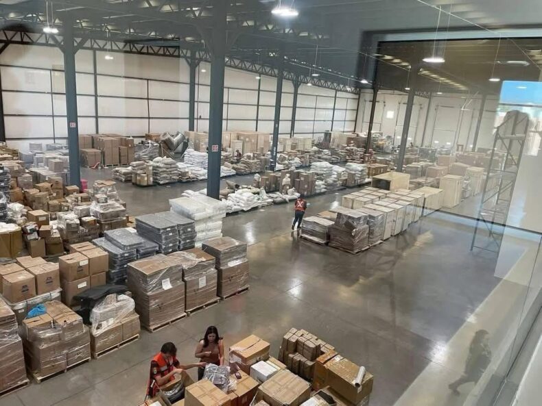 View of Vital Health Global’s warehouse with employees and palletized product inventory.