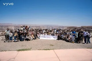 Large Vyvo group poses with banner at scenic desert canyon overlook under clear blue skies.