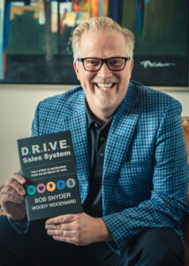 Woody Woodward holding DRIVE Sales System book on leadership and sales psychology